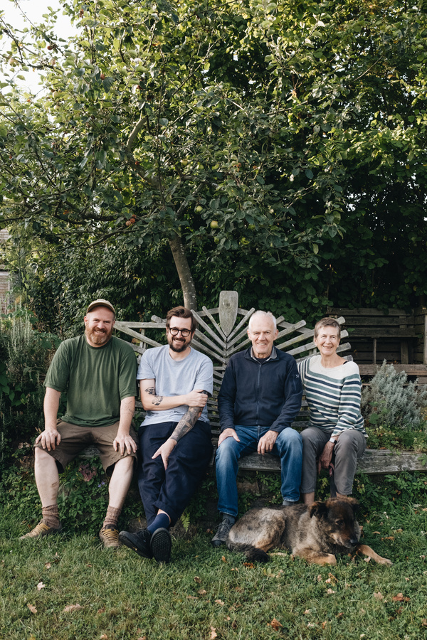 KI generiert: Vier Personen und ein Hund sitzen auf einer Bank im Garten, umgeben von grünen Bäumen.