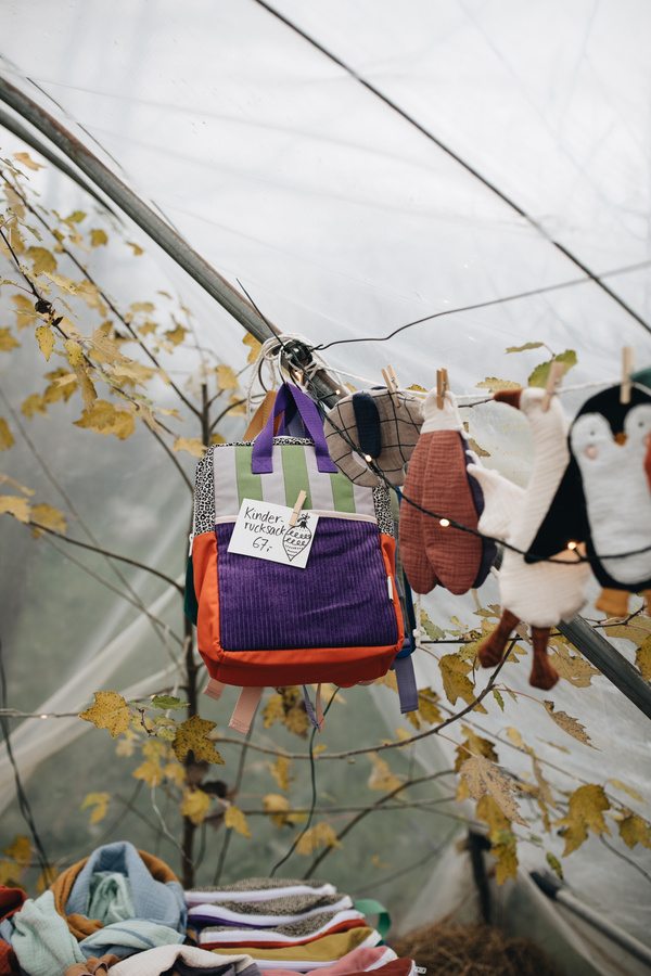 KI-generierte Beschreibung: Hauptinhalt: Kinderwagen mit Blumen und Stoffbeuteln. Text: "Kinderrucksack".