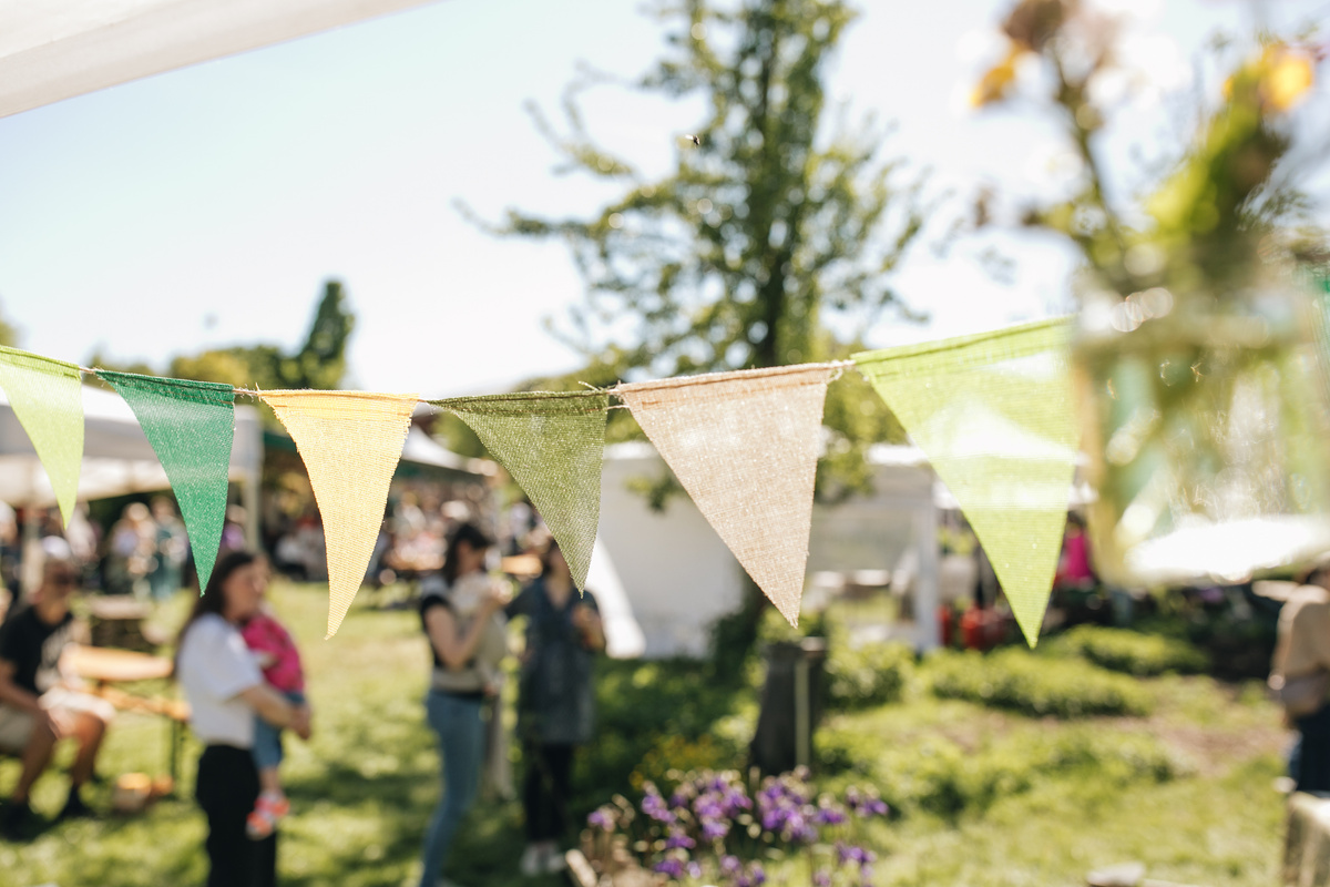 KI generiert: Bunte Wimpel bei einem Outdoor-Event im Park mit unscharfen Personen im Hintergrund.