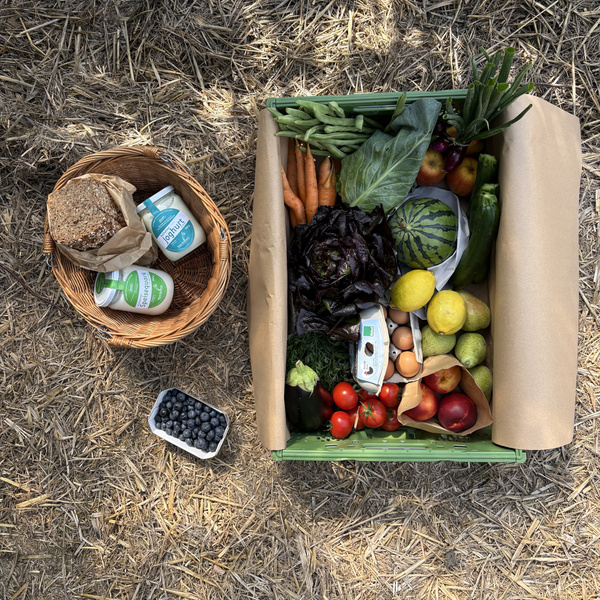 KI generiert: Eine Kiste mit frischem Obst und Gemüse, daneben ein Korb mit Brot und Joghurt.