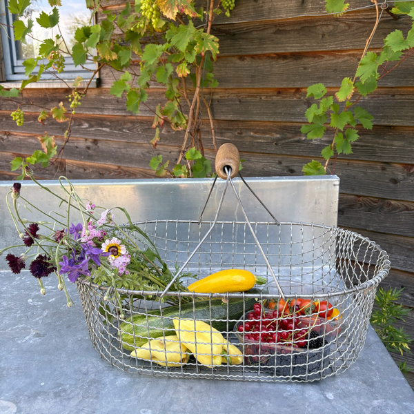 KI generiert: Ein Drahtkorb mit frischem Gemüse und Blumen vor einer hölzernen Wand mit grünen Ranken.