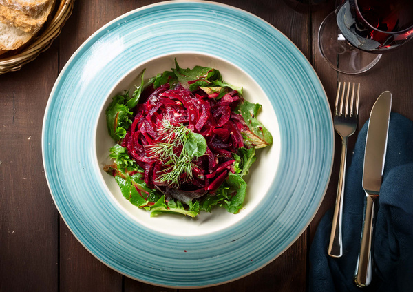 KI generiert: Ein Teller mit Rote-Bete-Salat auf einem Holztisch, daneben Brot und ein Glas Rotwein.