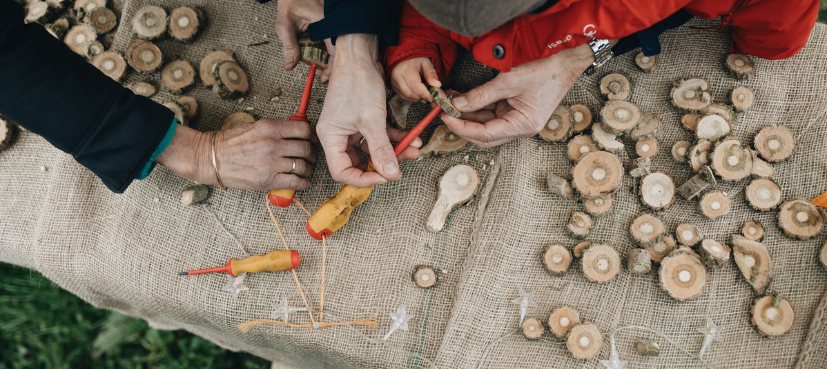 KI generiert: Hände bei einer handwerklichen Aktivität mit Holzscheiben und kleinen Werkzeugen auf einem Jutetuch.
