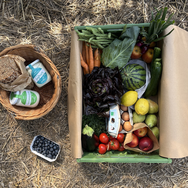 KI generiert: Eine Gemüse- und Obstkiste mit Brot, Joghurt und Heidelbeeren auf Stroh.