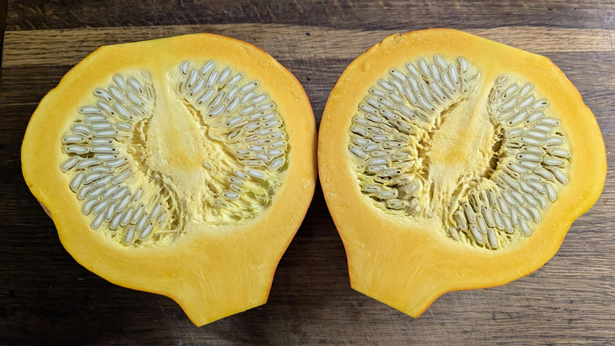 KI generiert: Ein aufgeschnittener Kürbis mit sichtbaren Kernen auf einem Holztisch.