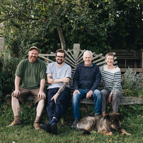 KI generiert: Vier Personen und ein Hund sitzen lächelnd auf einer Gartenbank vor grüner Kulisse.