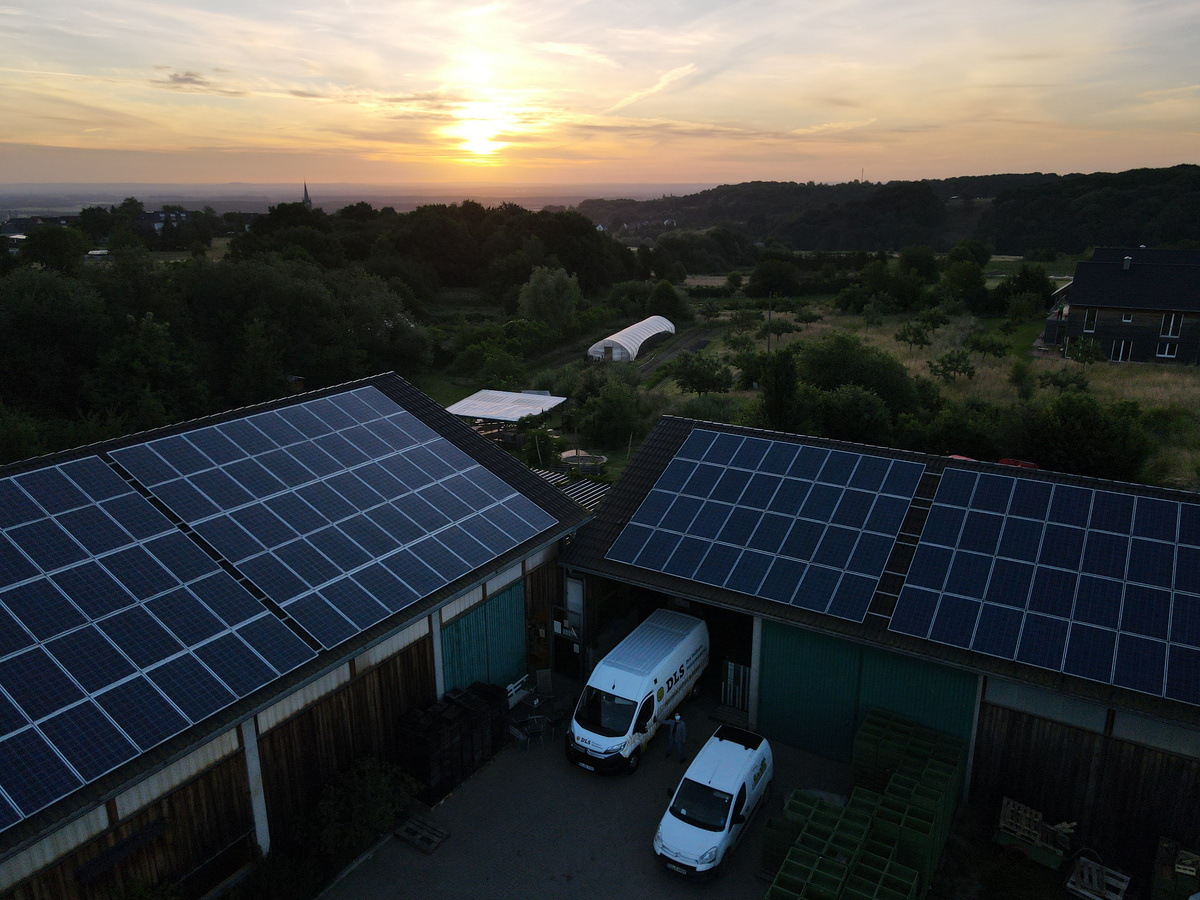 KI generiert: Gebäude mit Solarpanels bei Sonnenuntergang, umgeben von Landschaft und zwei Lieferwagen.
